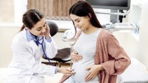 A gynaecologist listens to a pregnant woman's abdomen with a stetoscope.